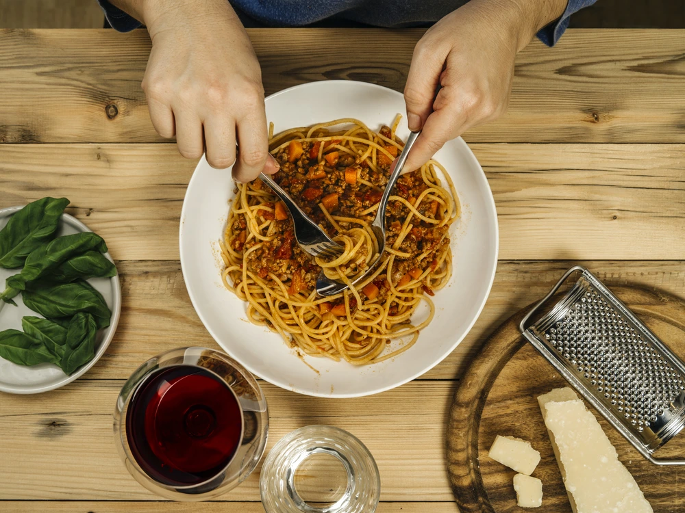 Plate of traditional spaghetti bolognese and glass of red wine on a wooden table